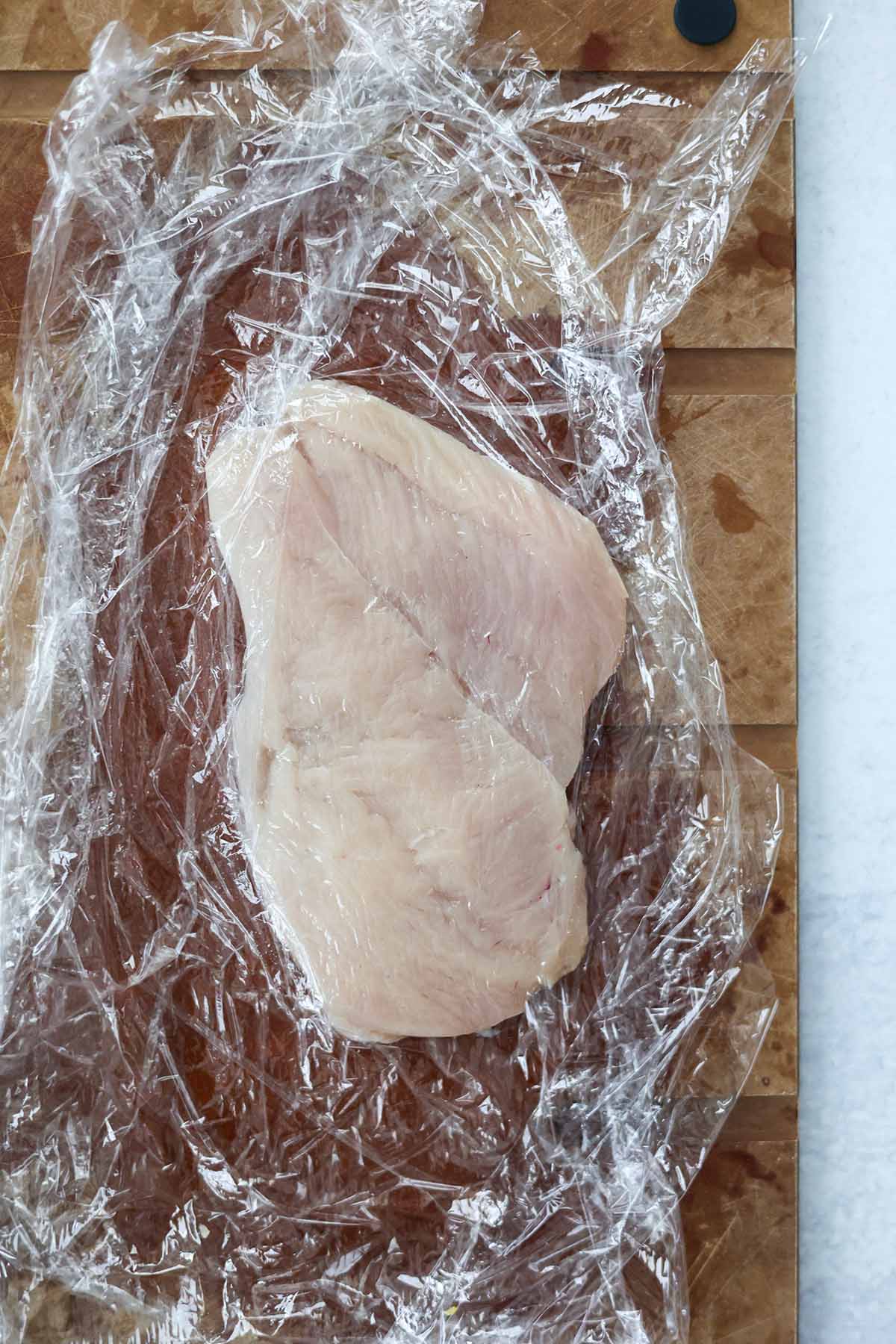 raw chicken breasts wrapped in plastic wrap. 