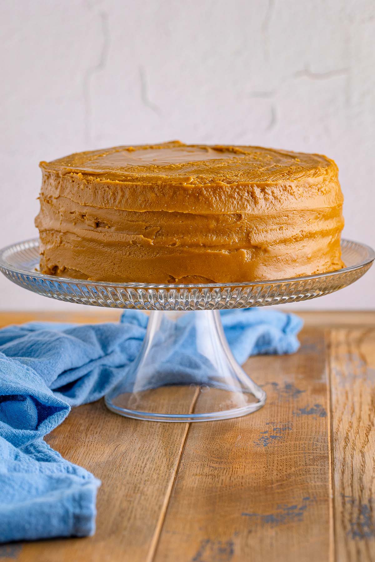 An entire frosted caramel two layer cake on a cake stand. 