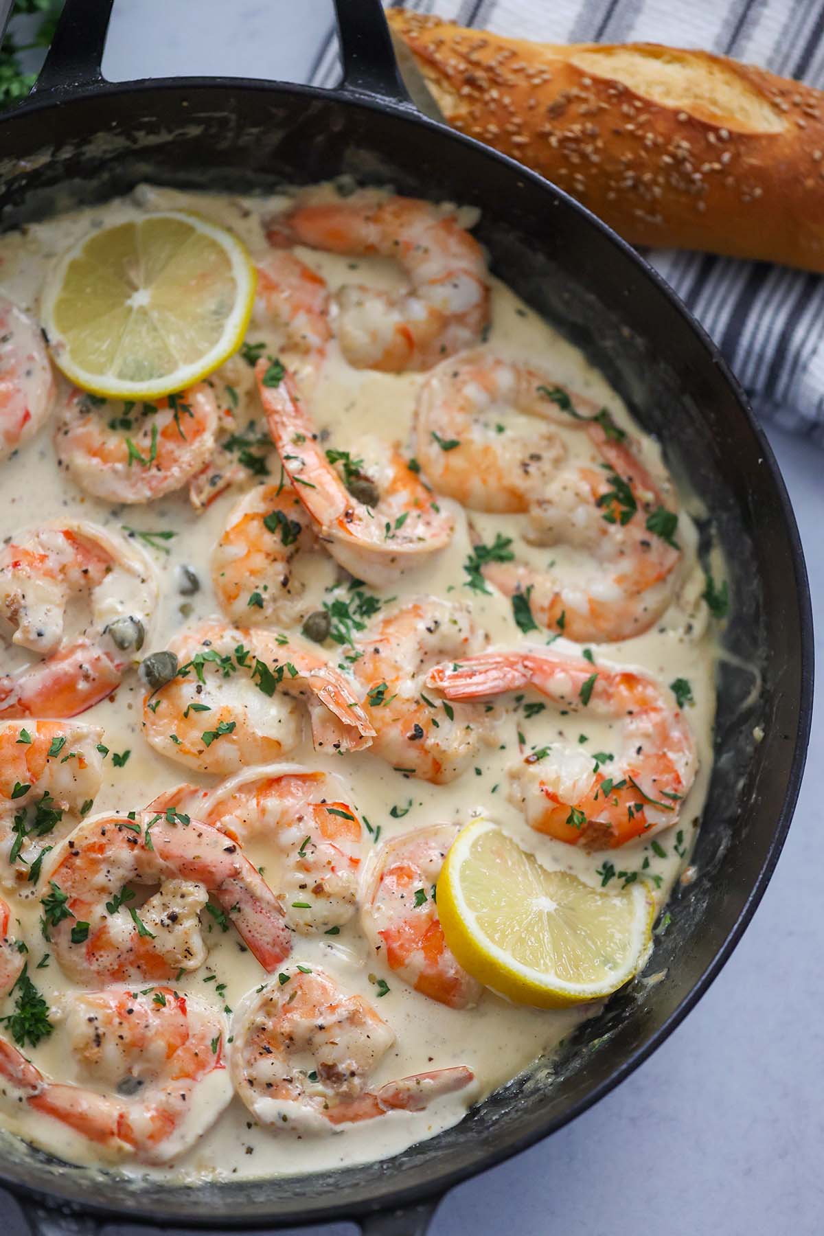 creamy shrimp piccata in a skillet with bread on the side. 