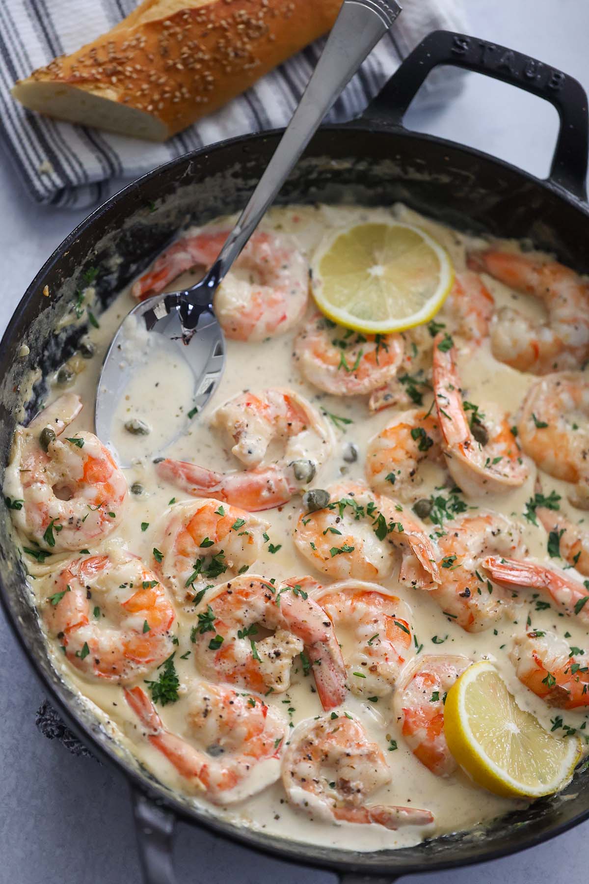 creamy shrimp piccata in a skillet with a spoon and lemon slices. 