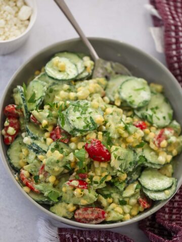 cucumber avocado tomato salad in a bowl with a spoon.