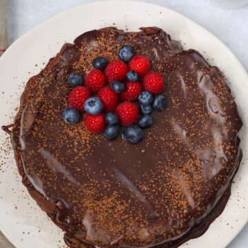 whole flourless chocolate cake with blueberries and raspberries on top.