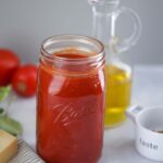 ultimate marinara sauce in a mason jar with olive oil and tomatoes in the background.