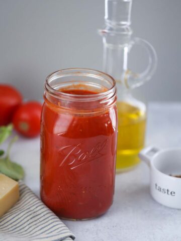 ultimate marinara sauce in a mason jar with olive oil and tomatoes in the background.