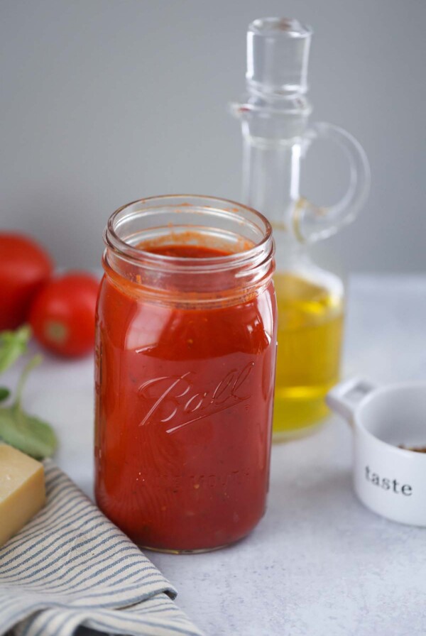 ultimate marinara sauce in a mason jar with olive oil and tomatoes in the background.