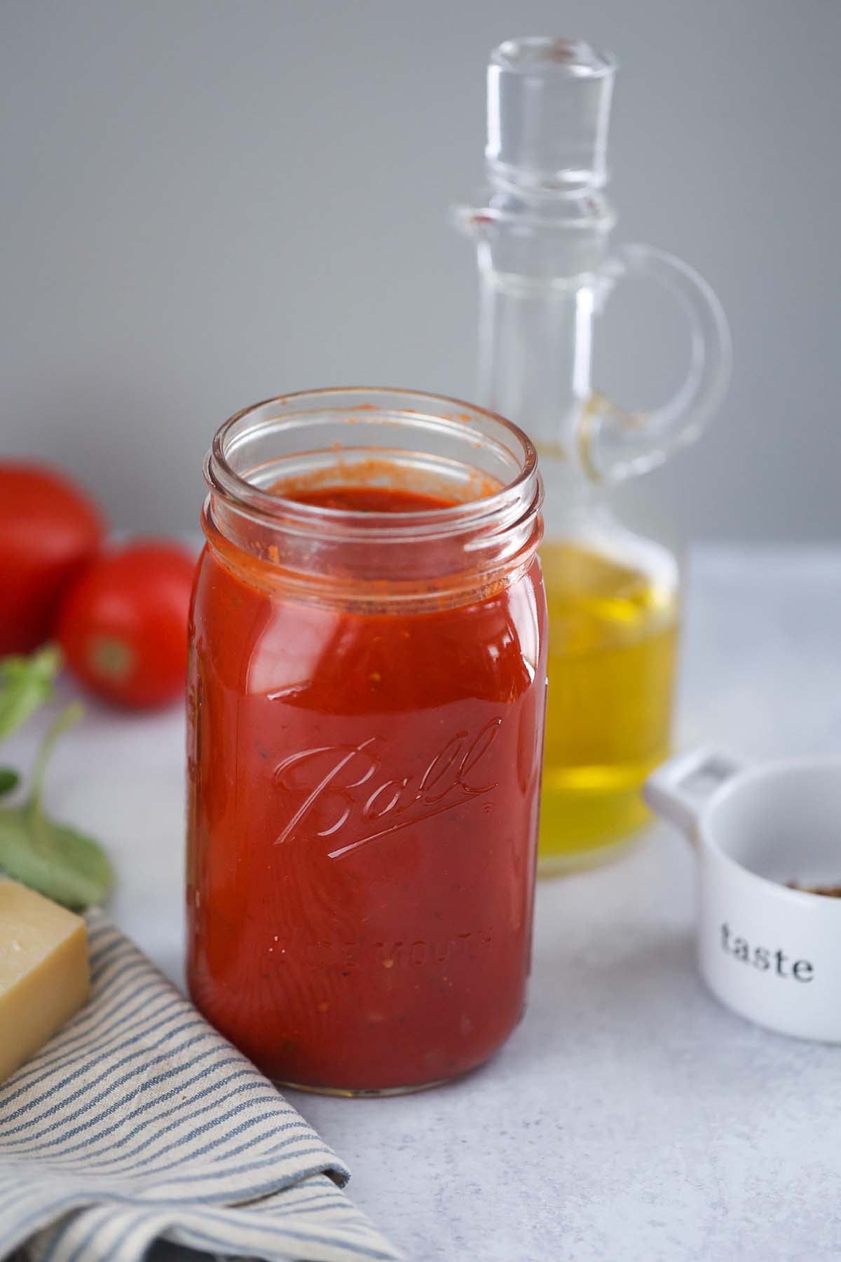 ultimate marinara sauce in a mason jar with olive oil and tomatoes in the background. 