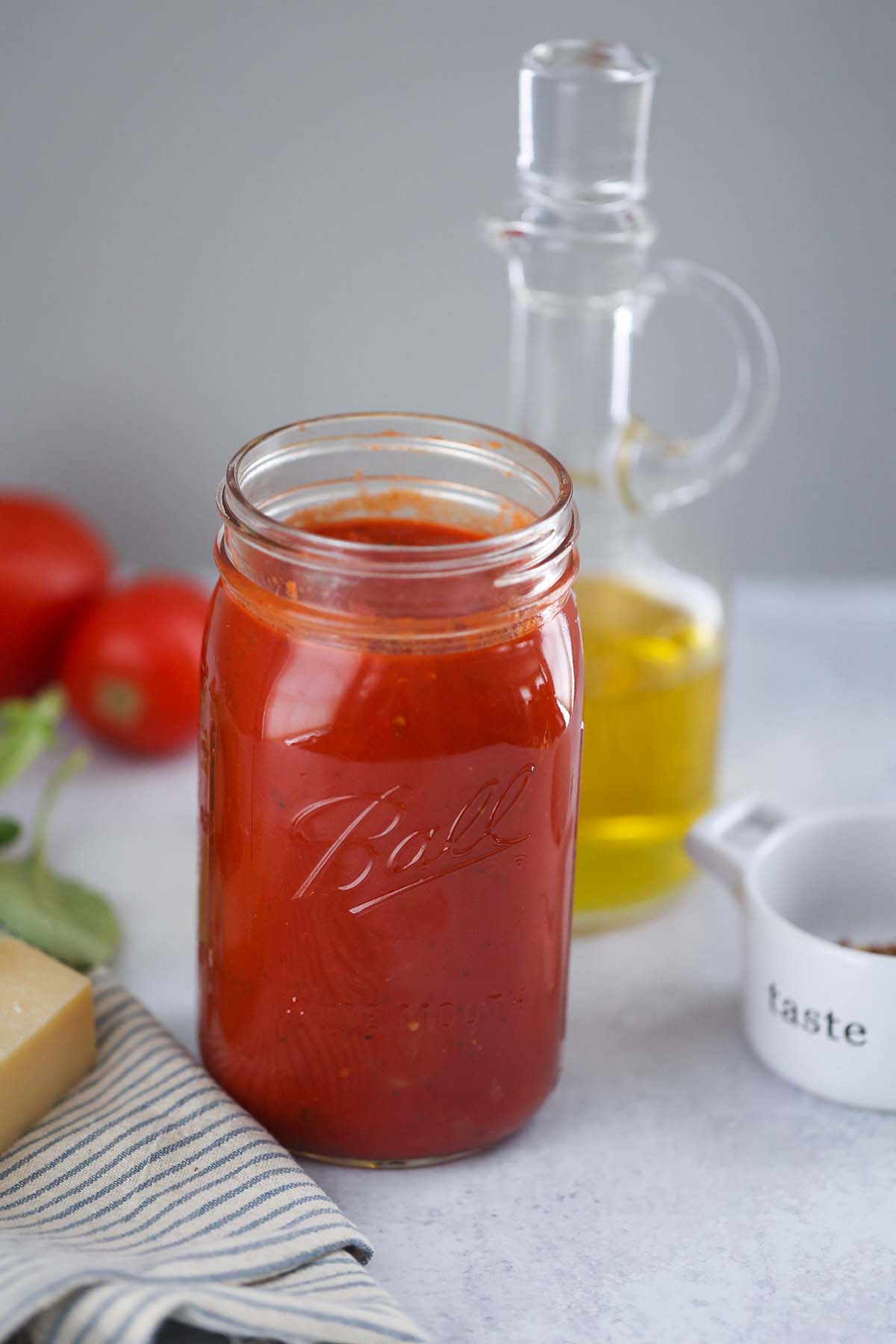 ultimate marinara sauce in a mason jar with olive oil and tomatoes in the background.