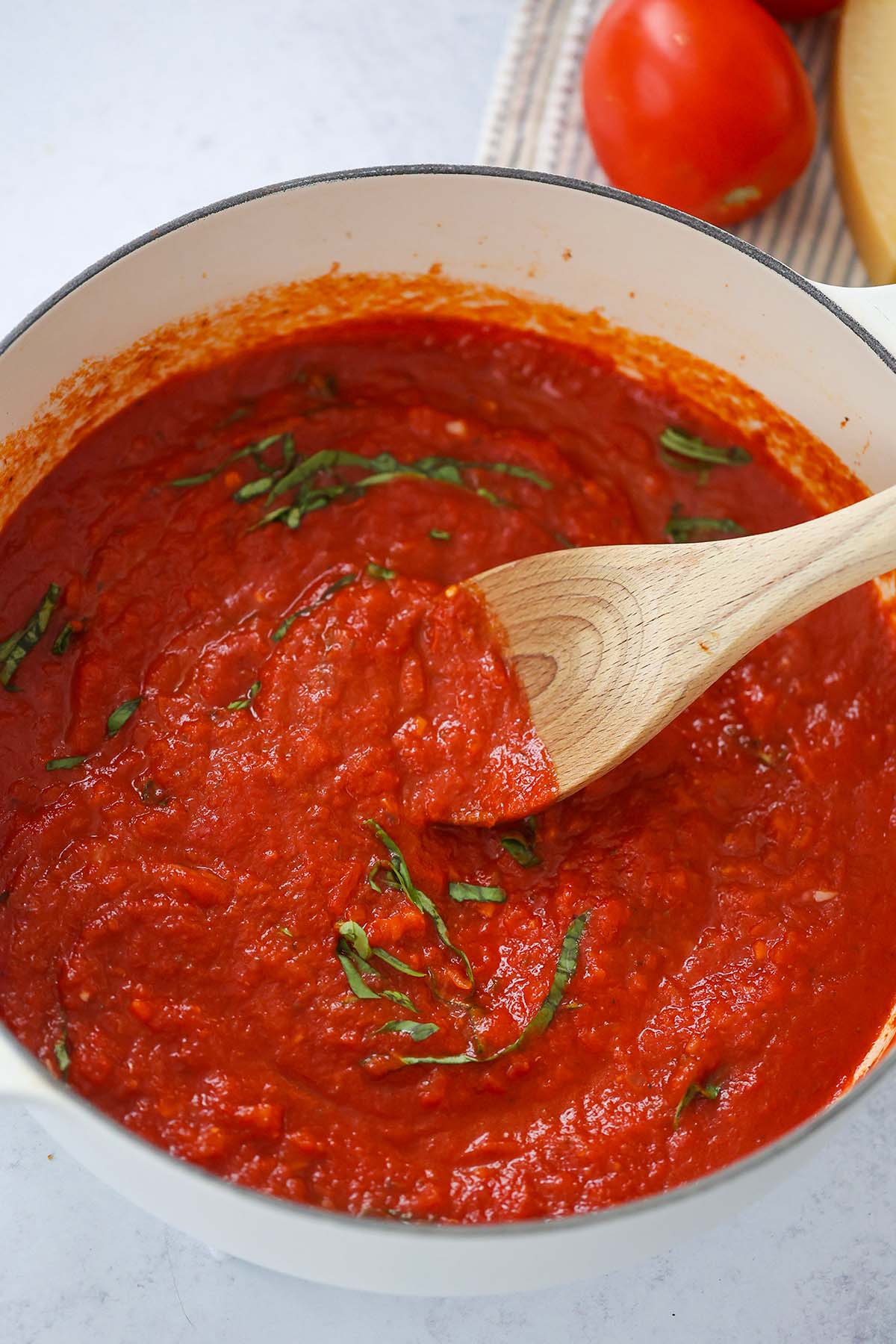 marinara sauce in a large pot with a wooden spoon and basil on top. 