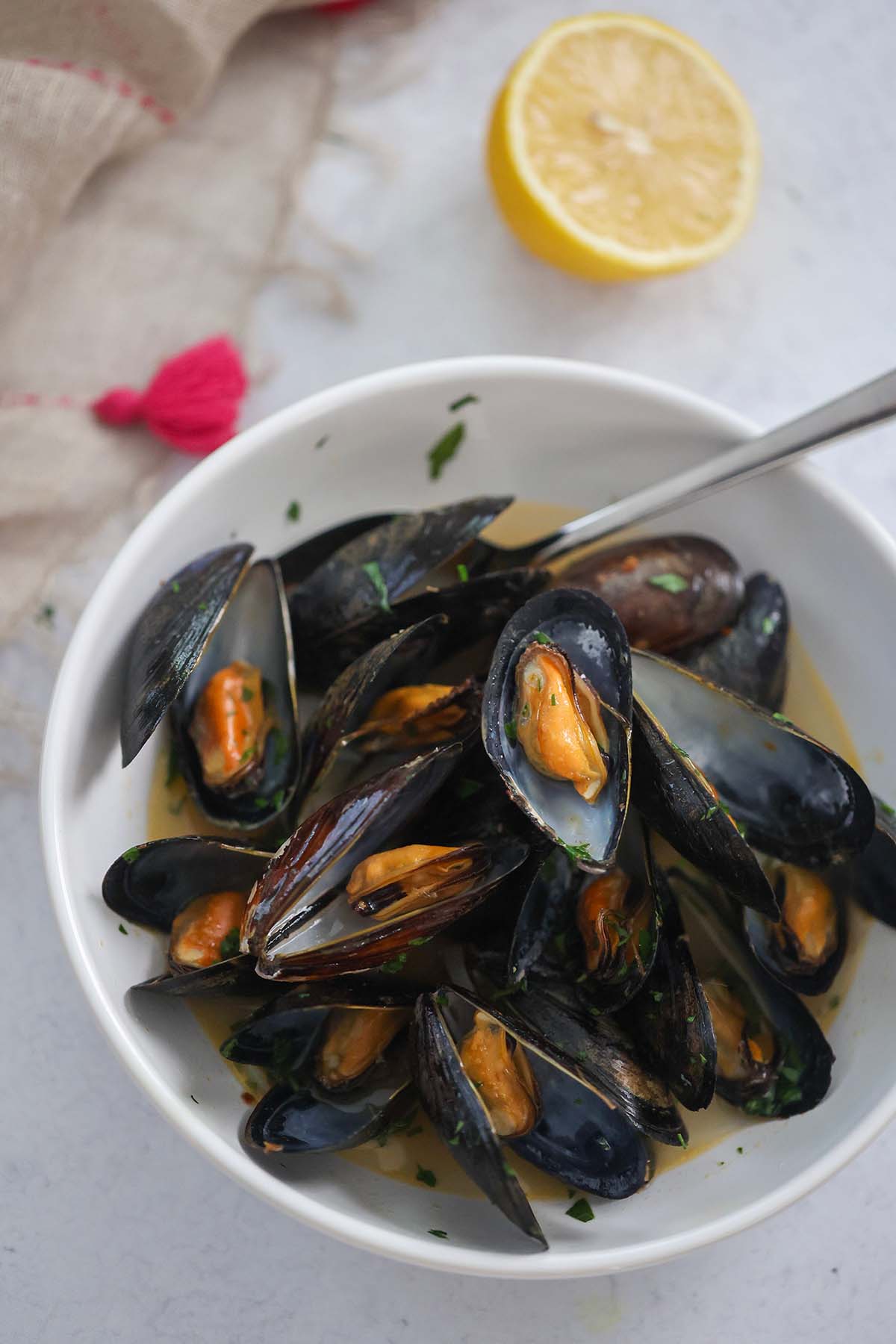 black opened mussels with a spoon in a white bowl with a lemon on the side. 