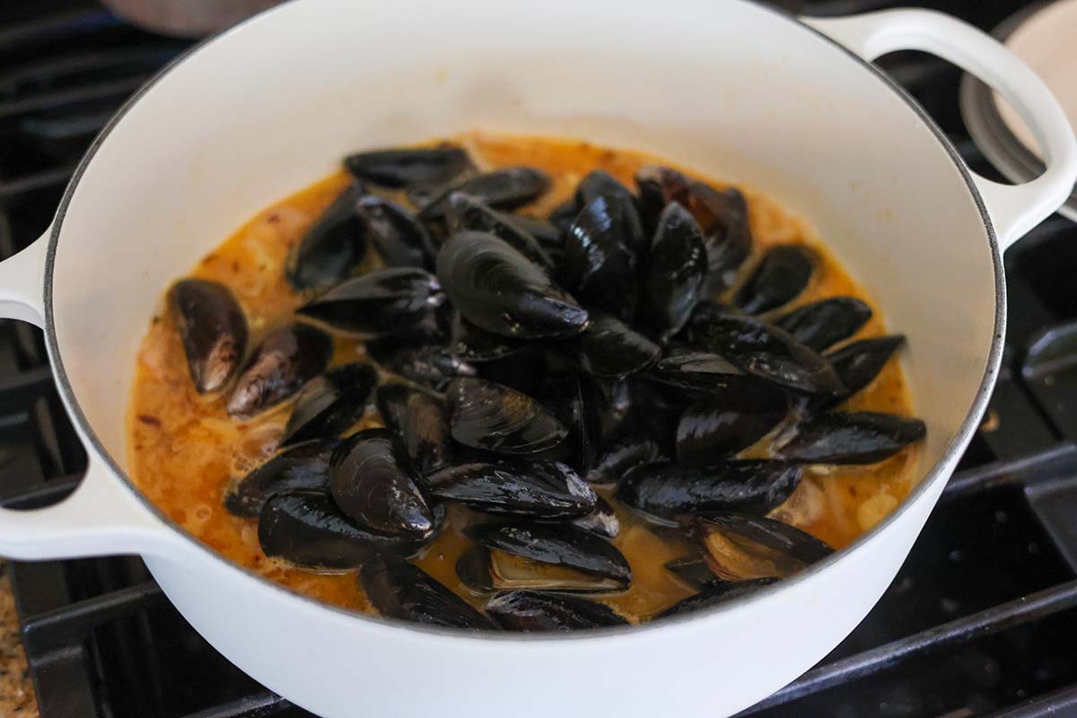black mussels and broth in a white pot. 