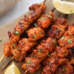 Pinchos de pollo on a wooden board with lemon wedges on the side.