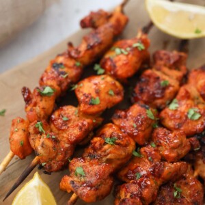 Pinchos de pollo on a wooden board with lemon wedges on the side.
