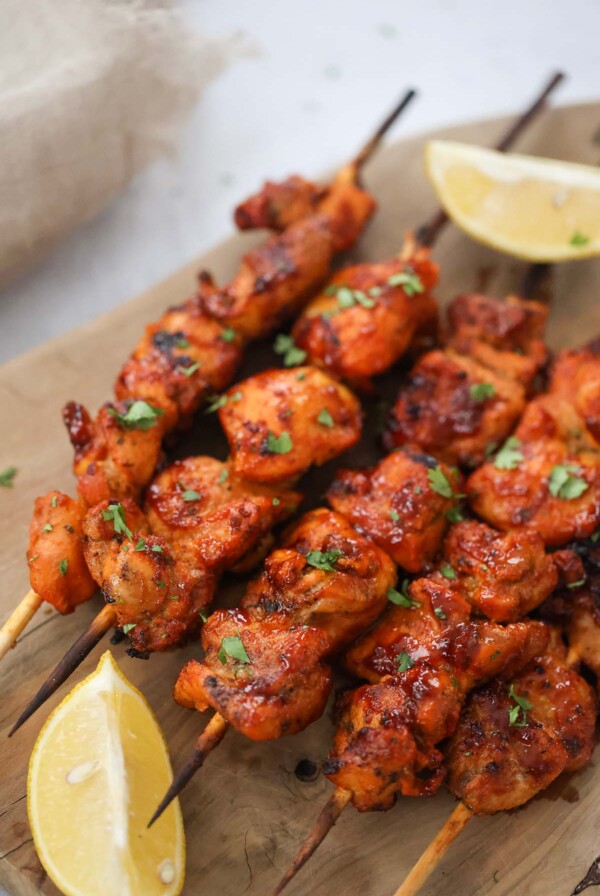 Pinchos de pollo on a wooden board with lemon wedges on the side.