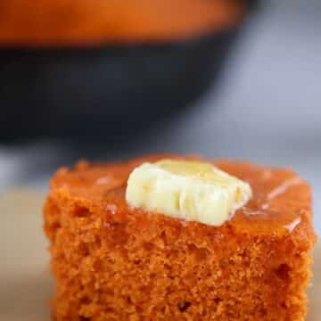 a square slice of sweet potato cornbread with butter and honey on top.