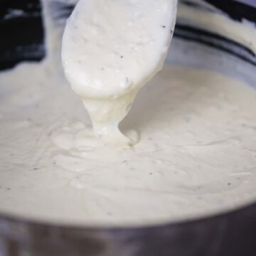 three cheese alfredo sauce in a skillet with a wooden spoon.