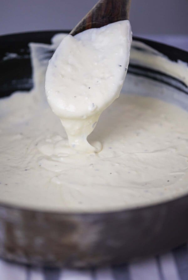 three cheese alfredo sauce in a skillet with a wooden spoon.