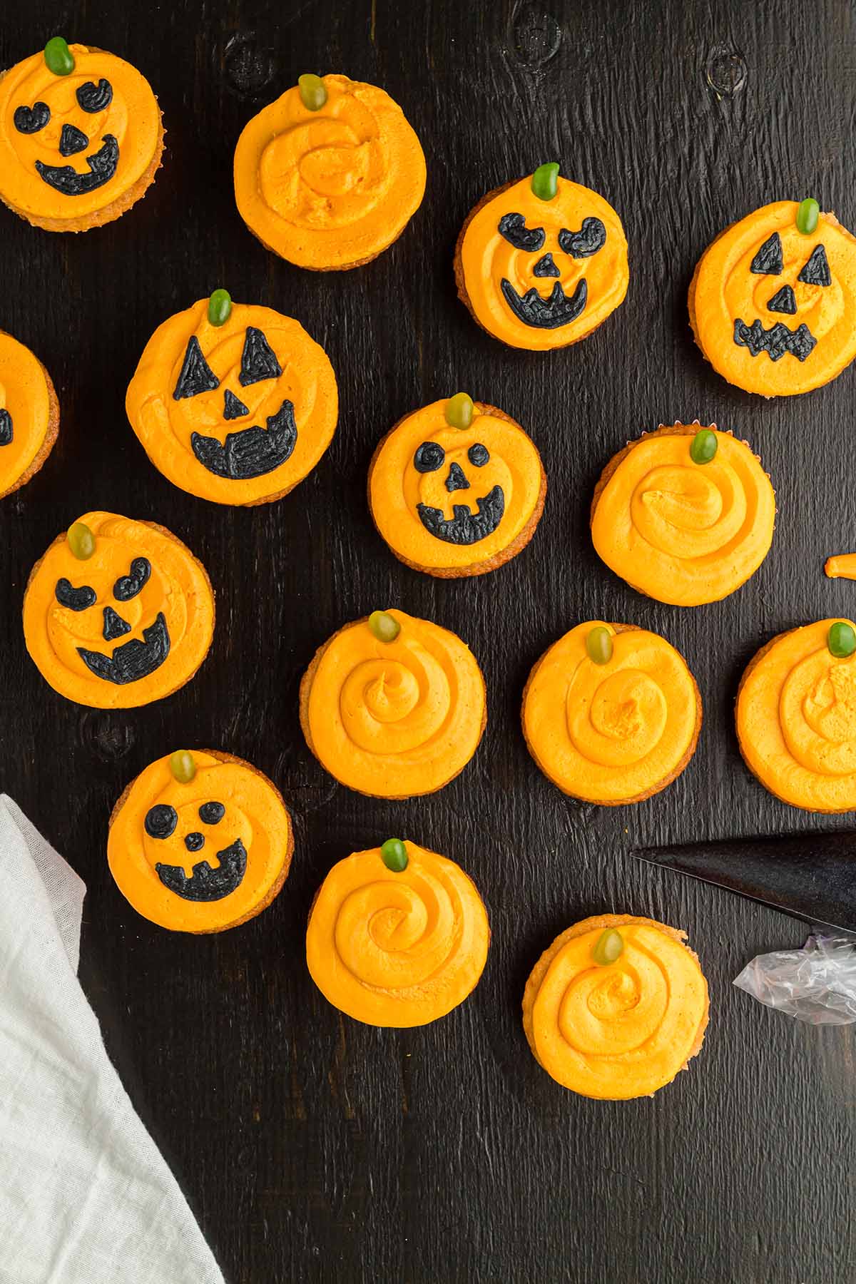 fifteen Jack O Lantern pumpkin cupcakes on a black surface. 