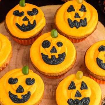 Seven Jack-O-Lantern cupcakes on a wooden board.