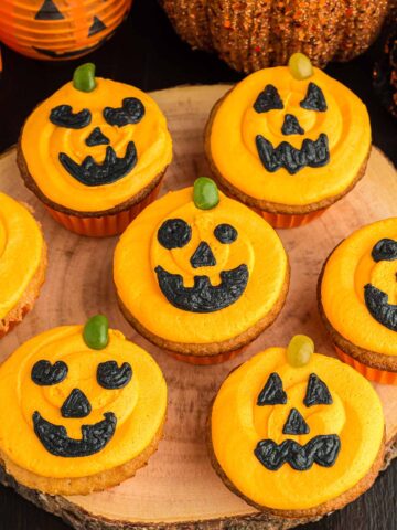 Seven Jack-O-Lantern cupcakes on a wooden board.