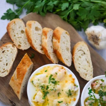 lobster cargot on a wooden board with bread and parsley on the side.