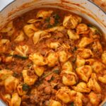 cheese tortellini with spinach and meat sauce in a pot.