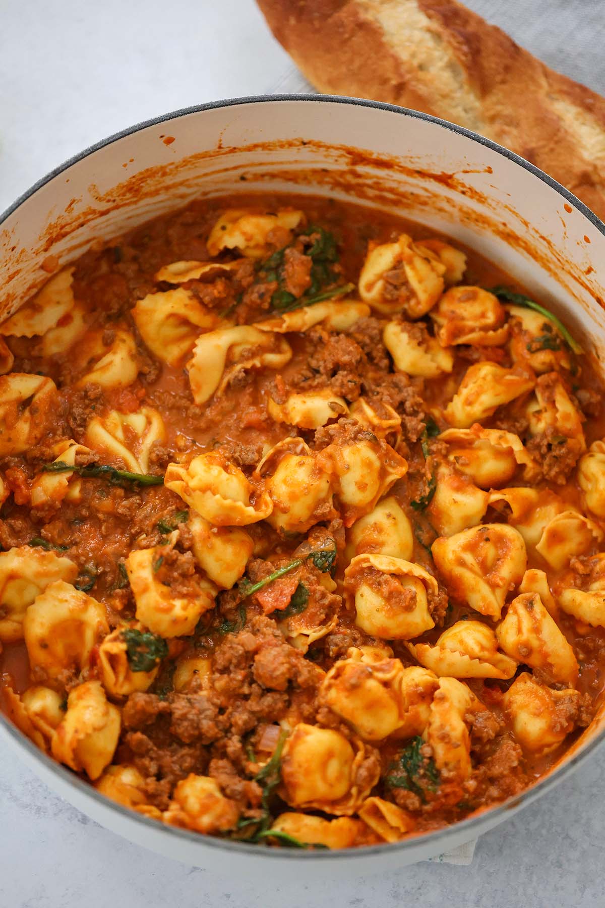 cheese tortellini with spinach and meat sauce in a pot.