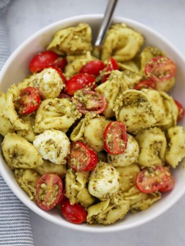 pesto tortellini salad in a bowl with a spoon.