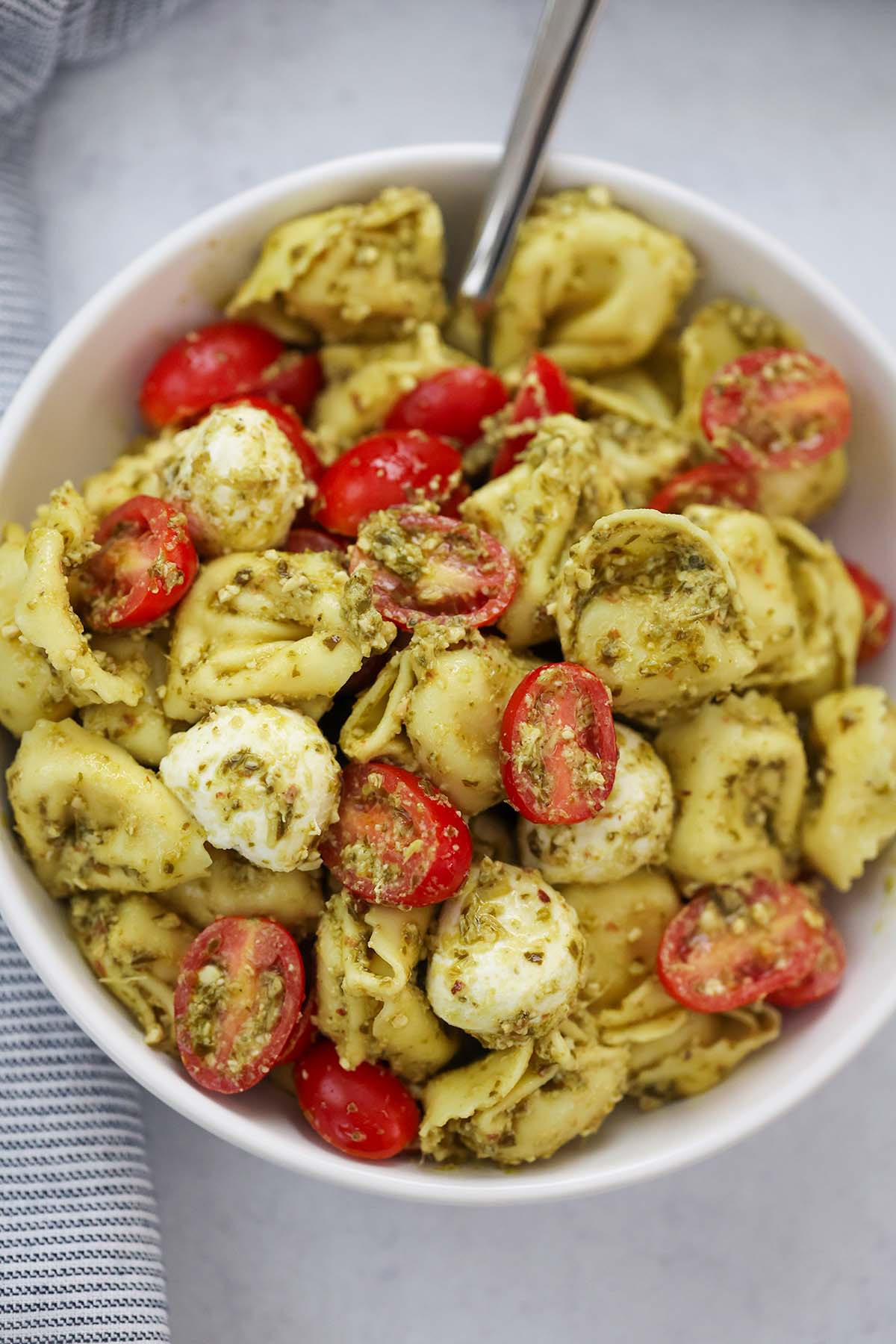 pesto tortellini salad in a bowl with a spoon. 