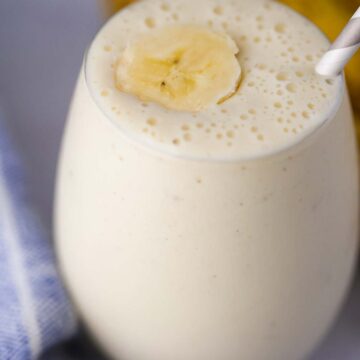 banana milkshake in a glass with a slice of banana on top and a straw.