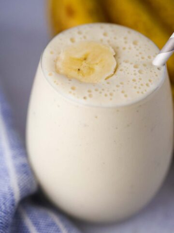 banana milkshake in a glass with a slice of banana on top and a straw.