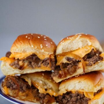 four cheeseburger sliders with caramelized onions on a plate.