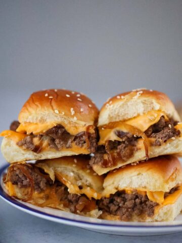 four cheeseburger sliders with caramelized onions on a plate.