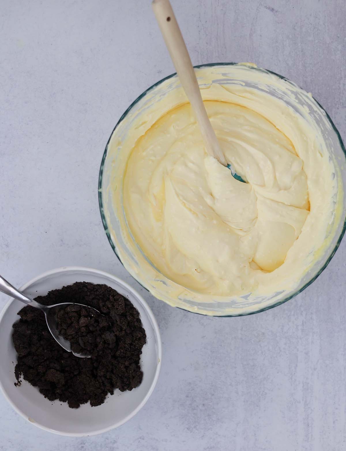 pudding mixture in a bowl with a spoon and crushed Oreo cookies in a separate bowl with a spoon.