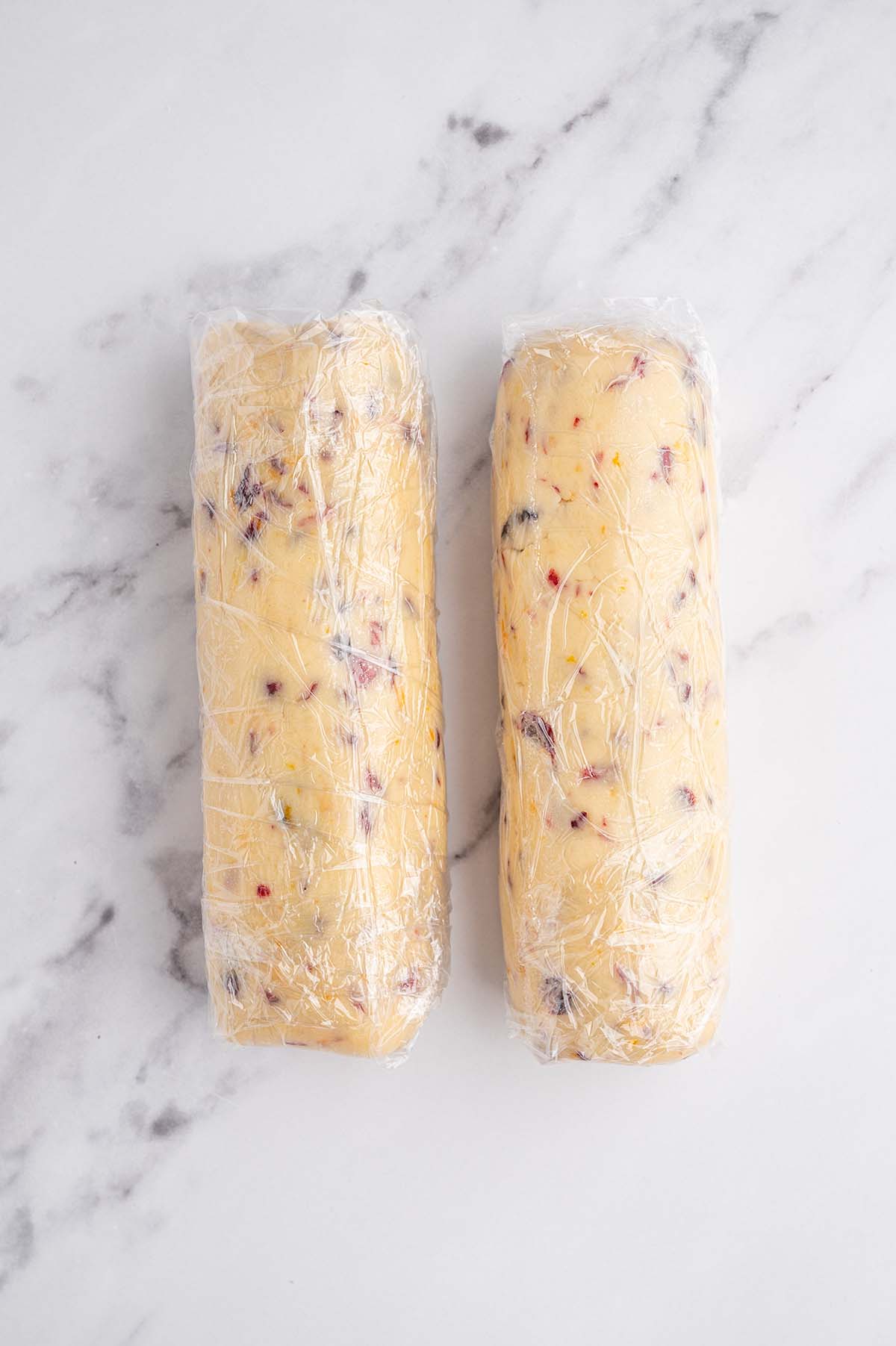 Two cookie dough logs wrapped in plastic. 