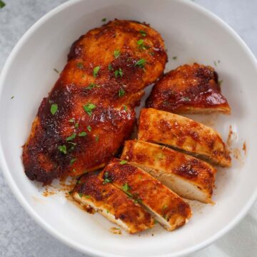 One whole bbq chicken breast and one sliced chicken breast on a plate.