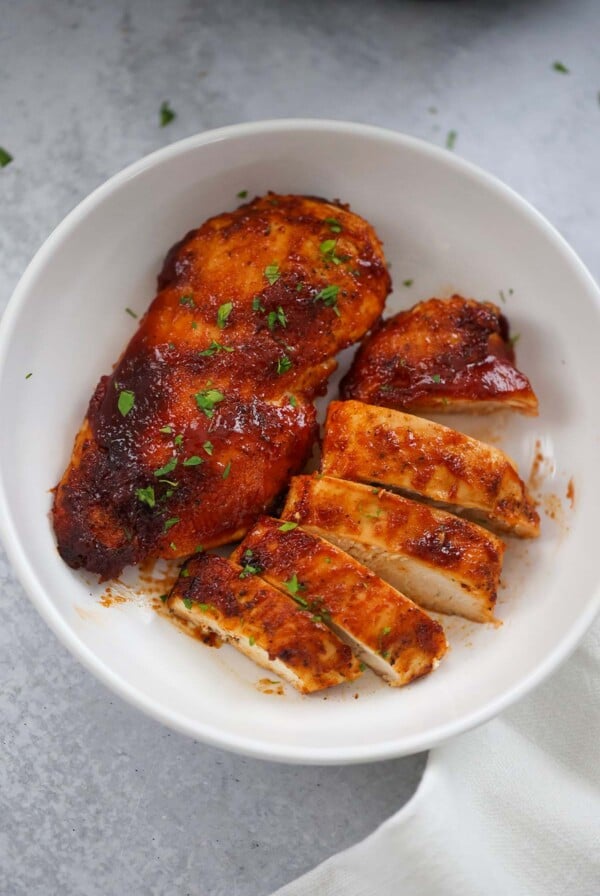 One whole bbq chicken breast and one sliced chicken breast on a plate.