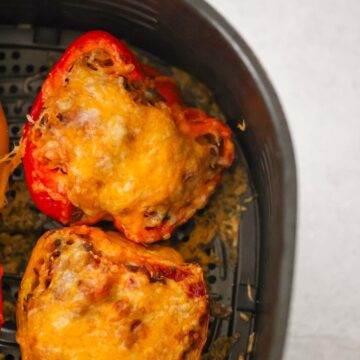 Two stuffed peppers in the air fryer basket up close.