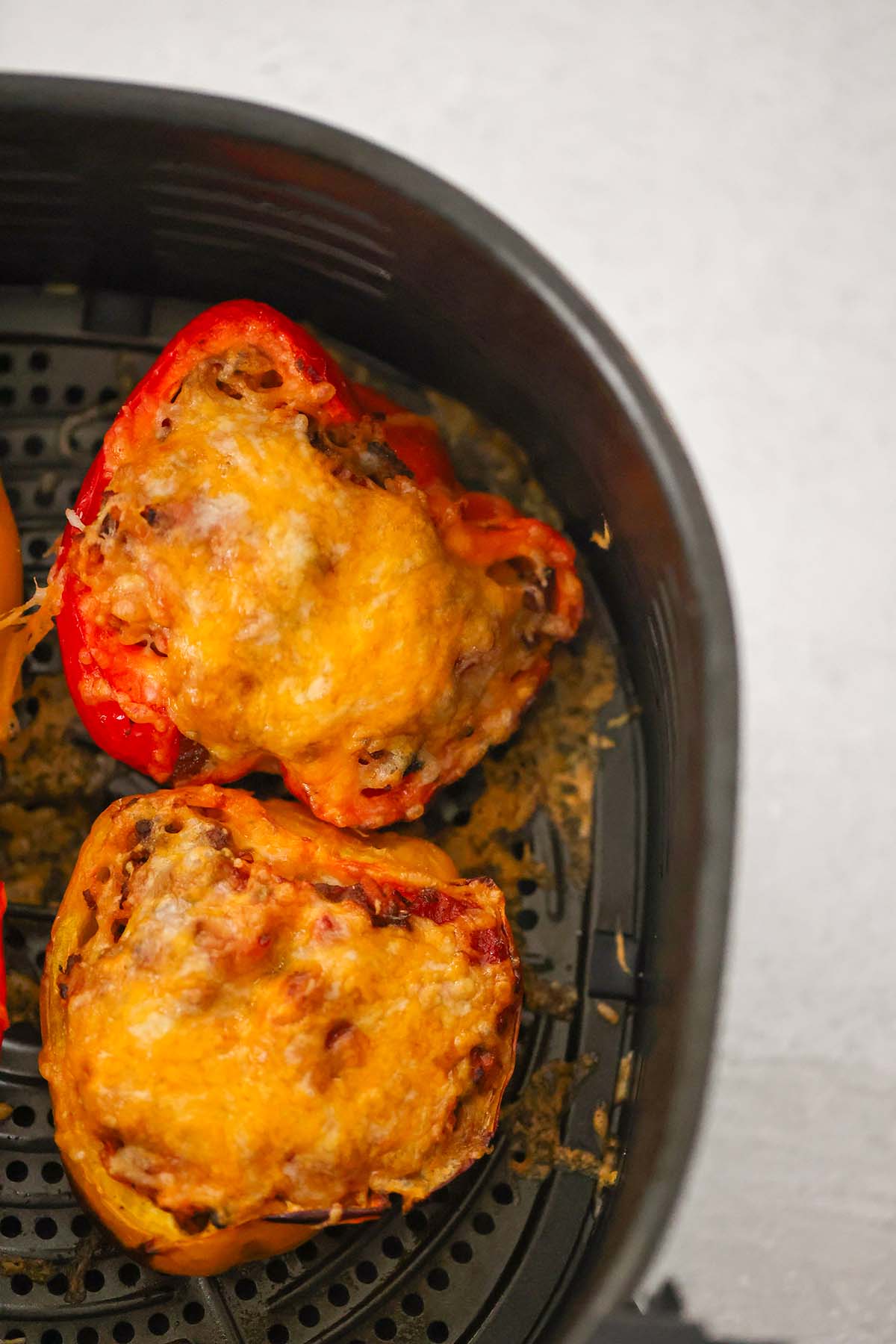 Two stuffed peppers in the air fryer basket up close. 
