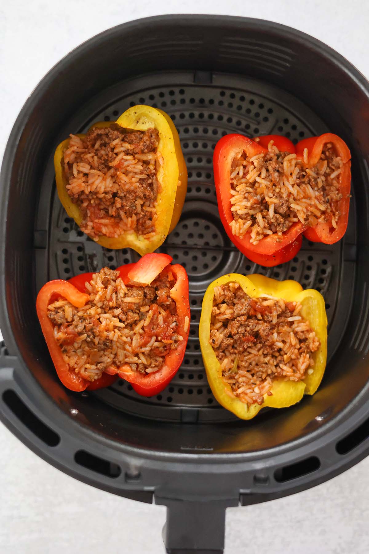 four stuffed peppers in the air fryer basket. 