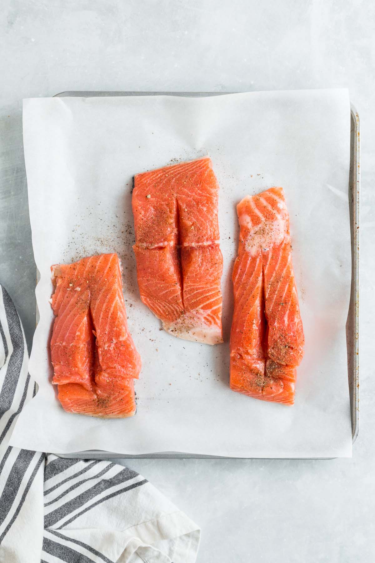 Three raw salmon fillets on a baking sheet with a slit in the center. 