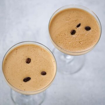 Two espresso martinis with foamy tops and coffee beans.