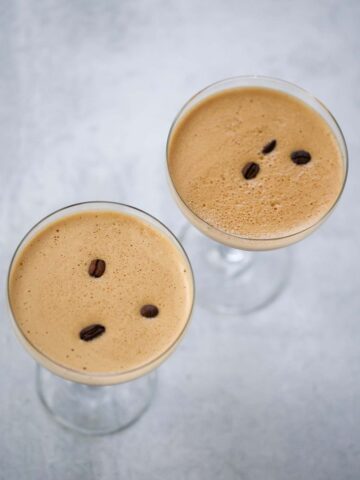 Two espresso martinis with foamy tops and coffee beans.