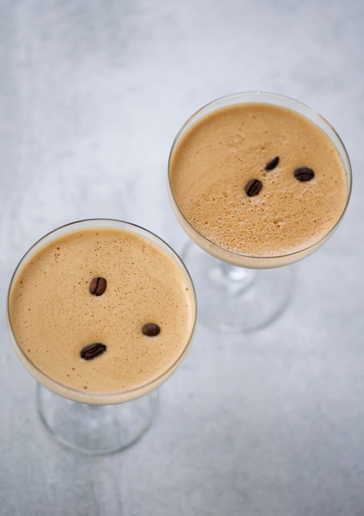Two espresso martinis with foamy tops and coffee beans. 