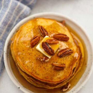 a stack of sweet potato pancakes with pecans, butter, and maple syrup.