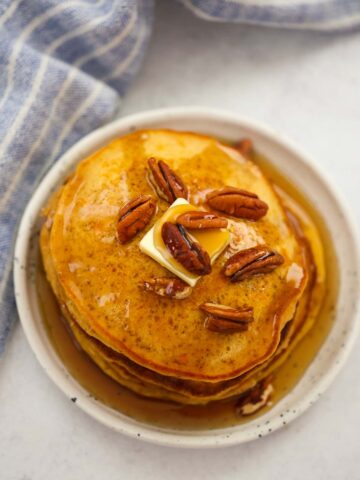 a stack of sweet potato pancakes with pecans, butter, and maple syrup.