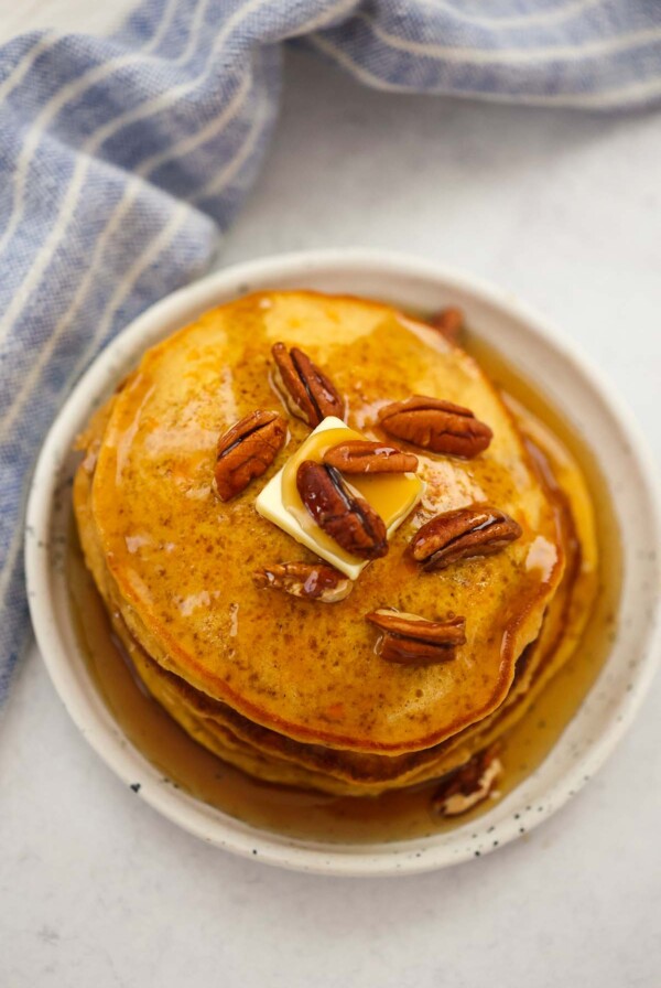 a stack of sweet potato pancakes with pecans, butter, and maple syrup.