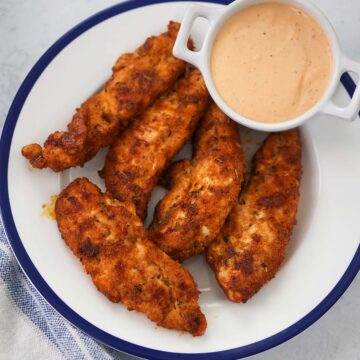 five baked chicken tenders with sauce on the side.