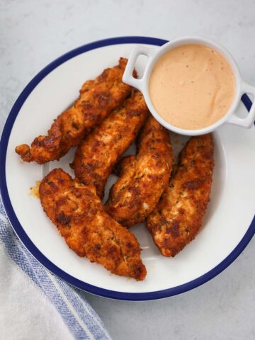 five baked chicken tenders with sauce on the side.