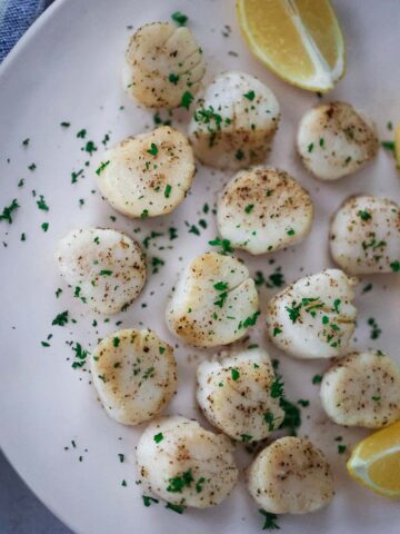 baked scallops on a plate with lemon wedges on the side.