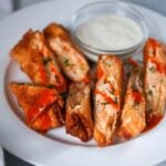 seven buffalo chicken egg rolls on a plate with ranch on the side.